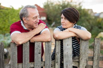 Elderly couple standing together near wooden fence in garden
