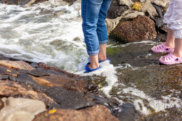 Woman's legs in slippers on the rocks near the sea.