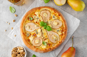 Delicious pizza with pears, gorgonzola cheese, walnuts and basil on a gray concrete background.