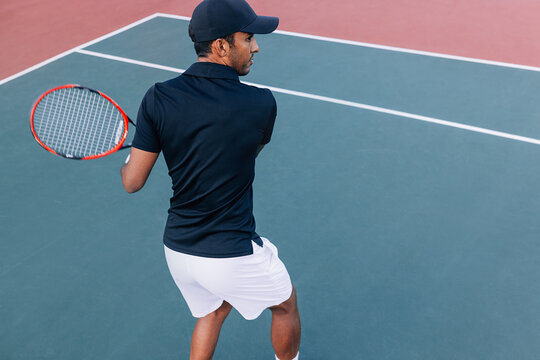 Back view of a male tennis player practicing a hard court outdoors