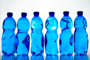 Transparent blue plastic bottles containing water, next to each other. Use and recycling of plastic, environmental protection.