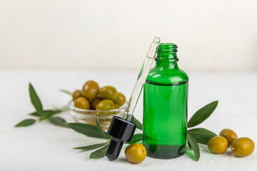 Olive essential oil. Glass bottle with olive oil on a texture table. Olive cosmetic oil. Serum for moisturizing and nourishing skin and hair. Beauty concept. Natural cosmetic. Copy space.spa