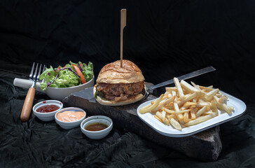 Pork burger with white sesame seeds with French fries potatoes and Salad served with ketchup sauce, mayonnaise and salad dressing on wooden cutting board. The concept of delicious food, Copy space.