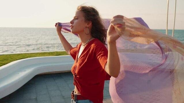 Pretty young woman rollerblading and holding scarf in the wind by the sea