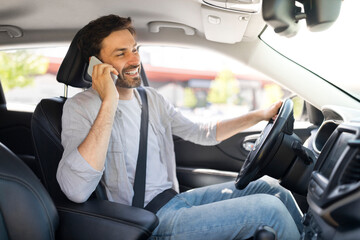 Cheerful young man driver talking on phone while driving car