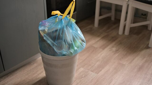 A trash can with a blue bag in the kitchen