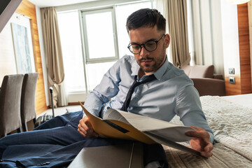 Fototapeta premium The businessman enters his hotel room, takes a seat, and then, with a sense of relief, sinks onto the hotel bed. The comfort of the room offers a well-deserved moment after a long day of meetings.