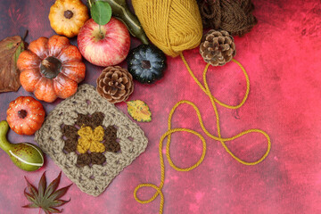Autumn crocheting. Top view photo of wool yarn balls, apples, squashes and leaves on red background with copy space. Coziness concept. 