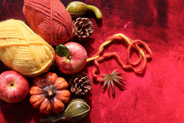 Autumn crocheting. Top view photo of wool yarn balls, apples, squashes and leaves on red background with copy space. Coziness concept. 