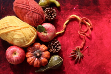 Autumn still life with pumpkins, apples and yarn on red background with copy space. Autumn crochet ideas. Cozy home concept. 