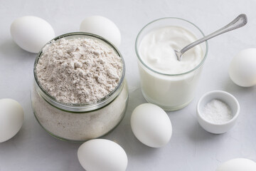 Ingredients for homemade rye pies with egg: rye flour, sour cream or yogurt and eggs on a light gray background - 647347331