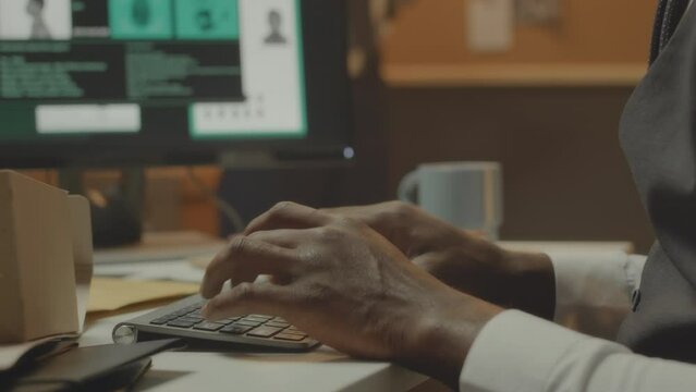 Unrecognizable male hands of detective agent typing on keyboard while filling in suspect data info in his profile, working on computer in office