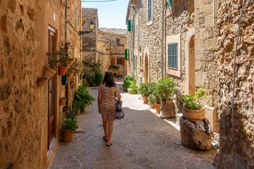 Fotobehang 50 year old woman with gray hair walking through the narrow and ornate streets of Valldemossa (Mallorca, Spain) on a sunny summer morning © Miguel Ángel RM