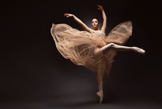 Ballerina. Young graceful woman ballet dancer, dressed in professional outfit, shoes and beige weightless skirt is demonstrating dancing skill. Beauty of classic ballet.