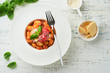 Potato gnocchi. Traditional homemade potato gnocchi with tomato sauce, basil and parmesan cheese on kitchen table on light grey kitchen table background. Traditional Italian food. Top view.