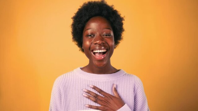 An African-American woman with curly hair opens her mouth in shock, showing the emotion of surprise, isolated against an orange background.