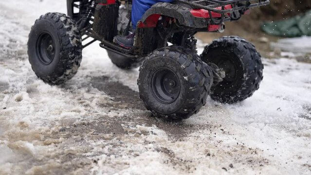 Atv shatter snow, ice and mud particles drifting on drive at slippery rural road in winter, slow motion