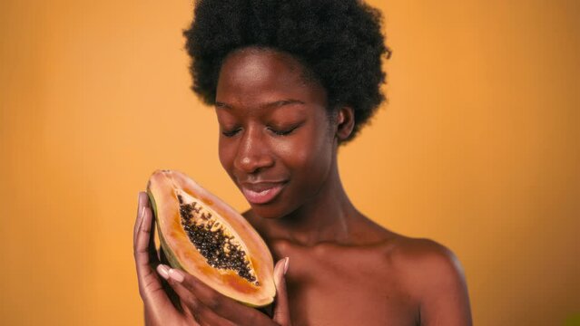 African American young woman with afro hair holding papaya in her hands isolated on orange background. Skin care and spa treatments.