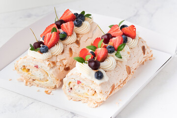 Homemade meringue roll decorated with almond flakes, blueberries and strawberries in the white gift box on the white background. Meringue roulade with whipped cream on top.