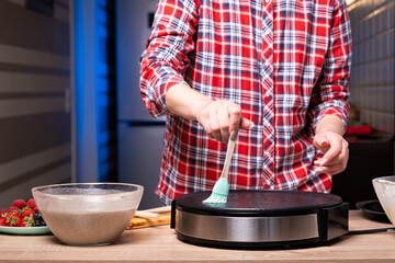 Woman cooking delicious crepe on electric pancake maker in kitchen, closeup