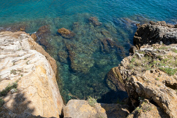 Image of the crystal-clear waters of the Mediterranean Sea in the Costa Brava, with the sun's reflection on its waves breaking against the rocks.