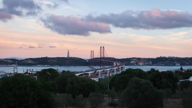 View of Lisbon view from Miradouro do Bairro do Alvito tourist viewpoint with Tagus river, traffic on 25th of April Bridge, and Christ the King statue at sunset. Lisbon, Portugal