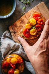 mano cogiendo una tostada con tomates cherry confitados