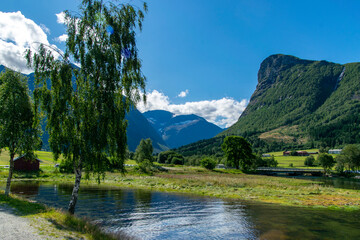Naklejka na ściany i meble Norway, idyllic scene with a lake among mountains and a traditional red rorbu house on a green meadow.