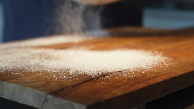 Wooden work surface with flour. Man's hand scatters flour through a sieve from above. Close-up.