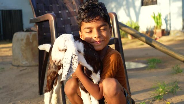 Indian child boy holding the small goat in flower fabric background. Pets animal and people concept.