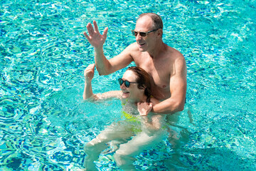 Happy mature family couple have fun in outdoor swimming pool enjoying vacation and freedom.