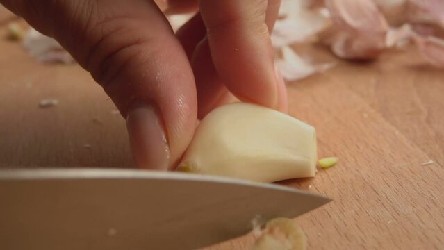 Close-up of hand cutting garlic cloves in the half on the wooden board on table