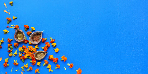 Diya lamps with marigold flowers on blue background with space for text. Divaly celebration