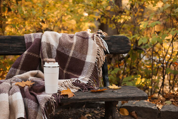 Cup of coffee with macaroon, fallen leaves and plaid on bench in autumn park