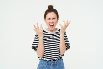 Image of angry woman shouts and shakes hands, stands in casual clothes over white background