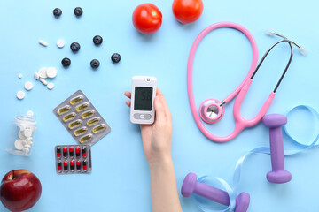 Diabetic woman with glucometer, pills, food, stethoscope and dumbbells on blue background