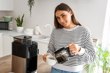 Young woman pouring coffee into cup in kitchen
