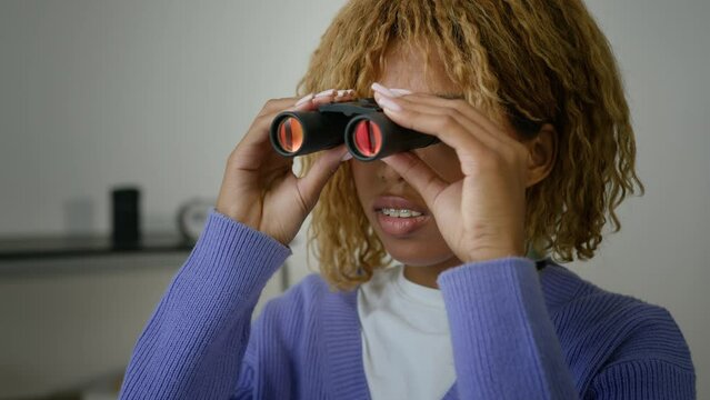 African American curious woman ethnic girl suspicious spy female at home indoors looking through binoculars spying gazing look watching in window secret observation contemplating jealousy girlfriend