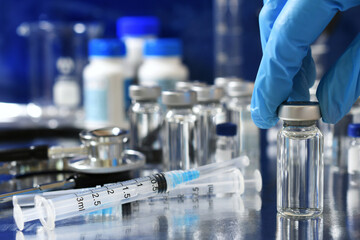 Medical personnel picking up vial of generic vaccine with more immunizations and syringes in...