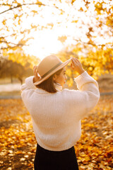 Beautiful woman in casual clothes and hat walking, enjoying the weather in the autumn golden park. Autumn mood. Fashion, style concept.