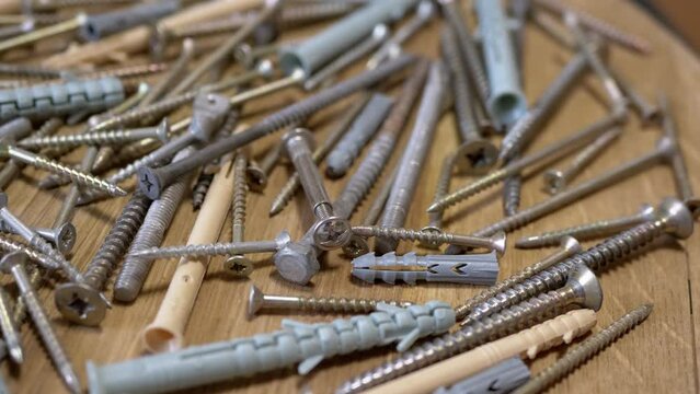 Lots of Scattered Stainless Steel Fasteners on a Rotating Wooden Background. Close up. An abundance of galvanized self-tapping screws with plastic dowels, screws, bolts, and washers. Selective focus.