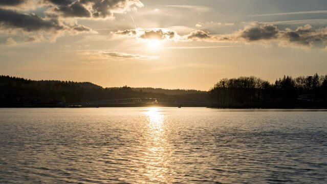 Sunset Timelapse with sunlight and sunrays obove Saint Pardoux Lake, france, Haute Vienne, Limousin, in April with orange water reflection