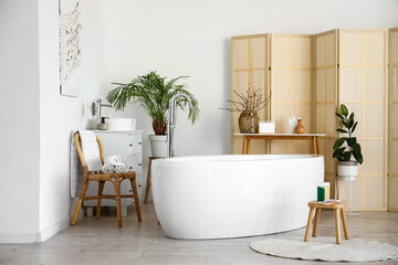 Interior of light bathroom with bathtub and folding screen