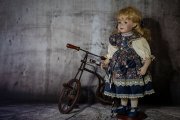 Realistic porcelain antique vintage girl doll or toy,  blonde hair and vintage dress with bicycle. Hand made