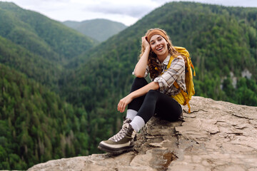 Naklejka na ściany i meble Beautiful traveler with a yellow hiking backpack observes the mountain scenery from a cliff, a view of the European troll tongue. Concept of nature, adventure, freedom.
