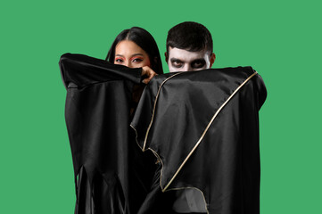 Young couple in costumes for Halloween party on green background