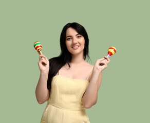 Beautiful happy young woman with maracas on green background