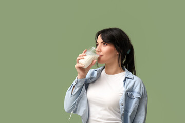 Pretty young woman drinking milk on green background