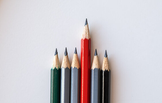 A red pencil standing out from the crowd of many identical gray brothers on a white background. Leadership, uniqueness, independence, think differently