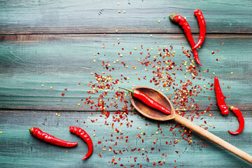 Red hot spicy cayenne peppers, both fresh and dried seeds, in wooden spoon. Flat lay over rustic background.